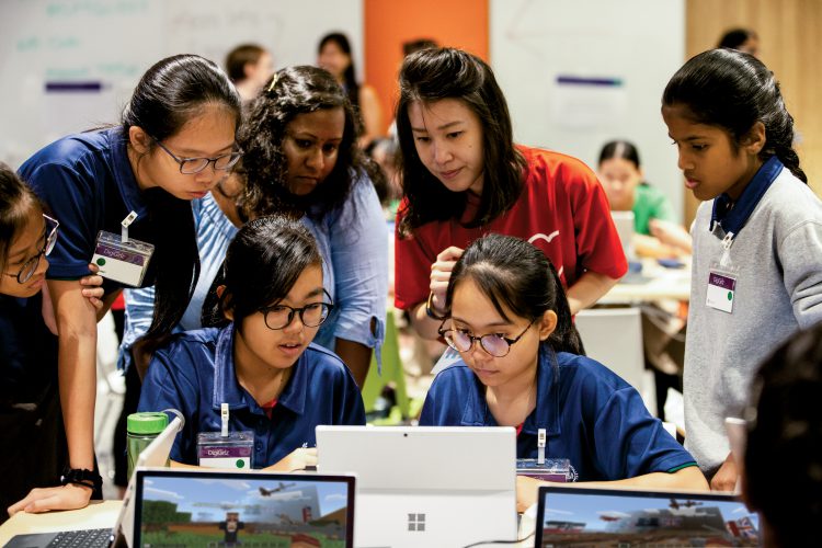 A group of female students cluster around a laptop.