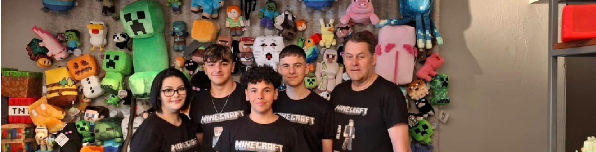 Students and teacher standing in front of a wall covered in Minecraft plushies