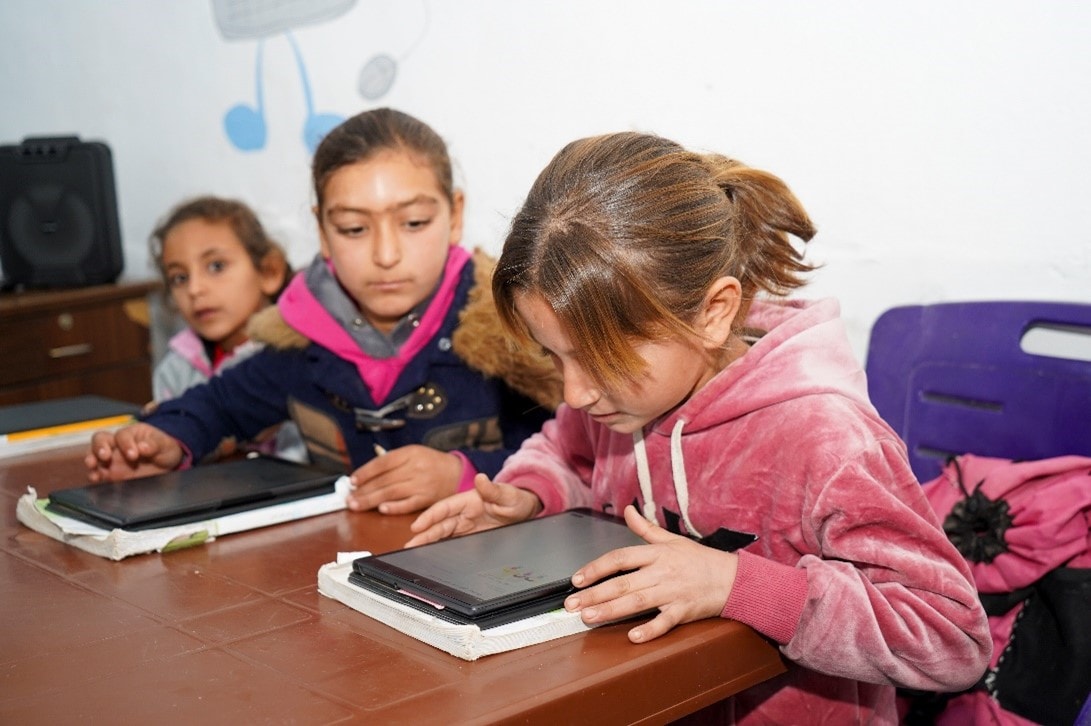 Three students at a desk, looking at devices