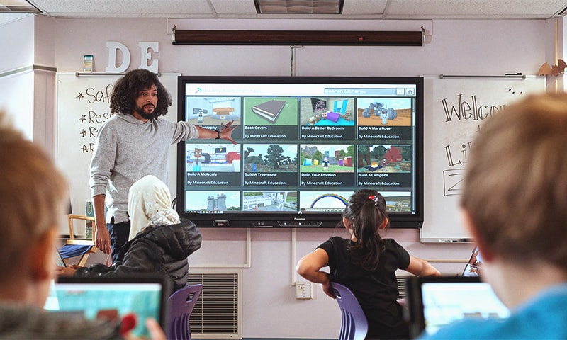 An instructor presents Minecraft lessons on a monitor in front of a classroom